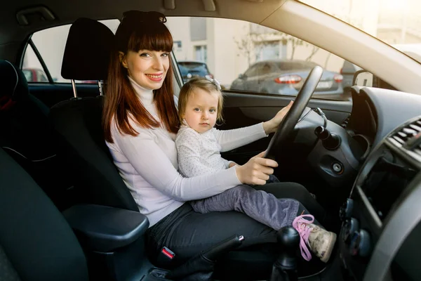 Mulher branca muito jovem, mãe com uma criança pequena estão sentados na frente do assento, enquanto o veículo parou. Mãe e criança sorrindo, se divertindo e brincando com a roda — Fotografia de Stock