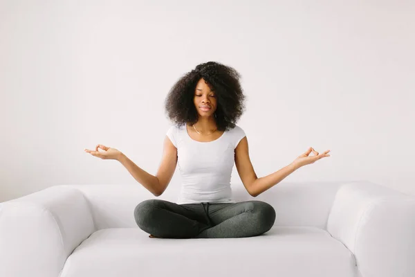 An African American young women sitting in the lotus position on white bed — Stock Photo, Image