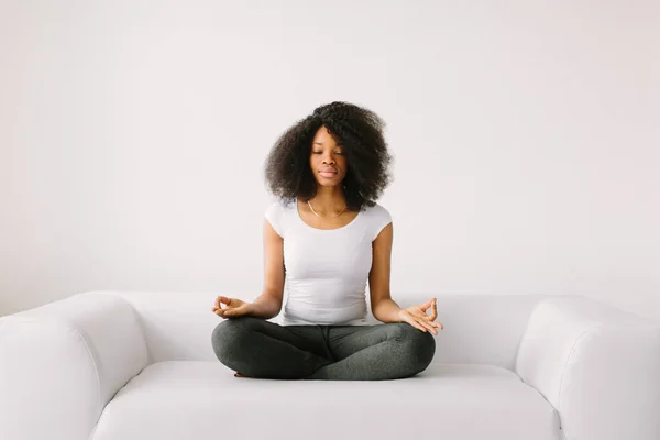 An African American young women sitting in the lotus position on white bed — Stock Photo, Image