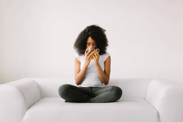 Una giovane donna afroamericana seduta nella posizione del loto sul letto bianco con una tazza di tè — Foto Stock
