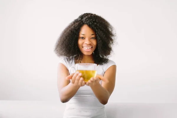 Una joven afroamericana sentada en la posición de loto sobre una cama blanca con una taza de té —  Fotos de Stock