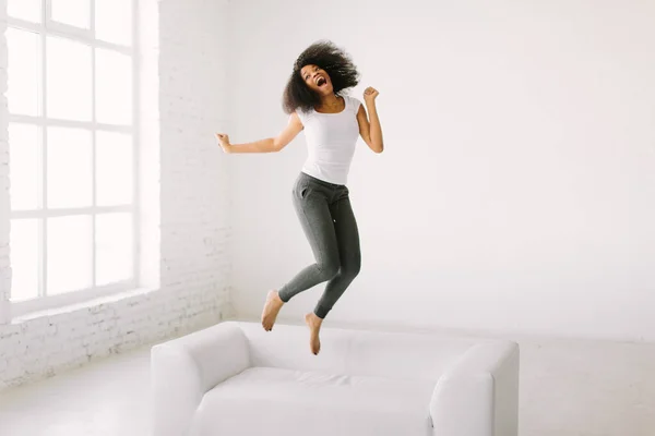 Μια Αφρο-Αμερικανίδα να πηδάει πάνω σε λευκό κρεβάτι. — Φωτογραφία Αρχείου