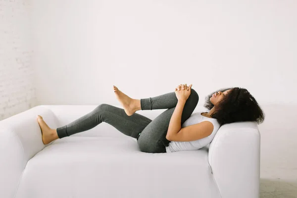 一位非洲裔美国女青年躺在一张白色的床上进行体育锻炼 — 图库照片