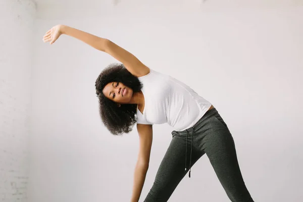 En afroamerikansk ung kvinna som står på en vit säng och motionerar. — Stockfoto