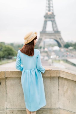 Mavi elbiseli ve şapkalı şık turist kadının Paris, Fransa 'da Eyfel Kulesi' ni gezerken arkadan görünüşü