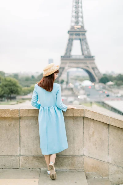 Bella ragazza caucasica che cammina vicino alle scale, Torre Eiffel sullo sfondo, Parigi. Affascinante signora in abito blu rimanendo di nuovo alla fotocamera e guardando la splendida vista di Parigi — Foto Stock