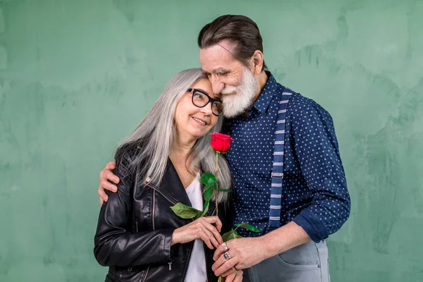 Love has no age. Romantic senior couple celebrating Saint Valentines Day. Beautiful woman and handsome man enjoying spending time together, embracing and holding red rose