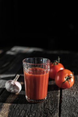 Koyu bir tahta üzerinde bir bardak taze domates suyu, domates ve sarımsak.