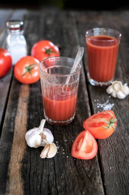 Koyu bir tahta üzerinde bir bardak taze domates suyu, domates ve sarımsak.