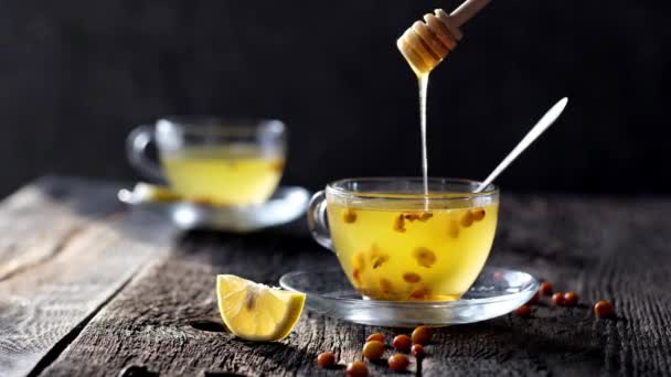 レモンと蜂蜜と新鮮な注ぐ海のクロウメモドキ茶のガラスは日当たりの良い光で暗い木製の背景に — ストック動画