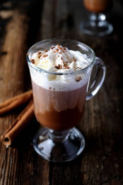 Tahta masa arkasında tarçın süslemeli bir fincan sıcak çikolata.