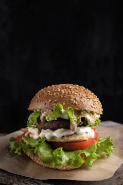 Salatadan taze yeşil yaprak, domates ve salatalıklı ev yapımı hamburger, siyah arka planda ahşap masa.