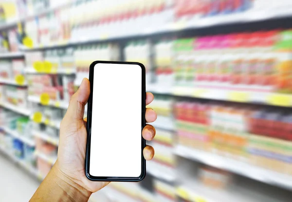 Mão segurando telefone inteligente para compras supermercado on-line com fundo de supermercado borrado. E-commerce e conceito de tecnologia . — Fotografia de Stock