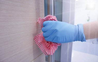 Kapalı el mavisi tıbbi eldivenler ve kapıyı temizlemek için antiseptik içeren bir bez kullanın. Virüs gribi ve Cvid-19. Sağlık konsepti..