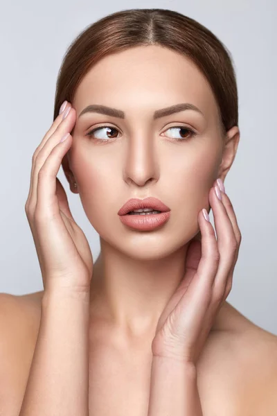 Beauty Woman Portrait. Front view spa model girl headshot. Pretty young woman touching her face. Skin care. Youth. Beautiful Fashion Model Girl Face. Perfect Skin. Grey Background