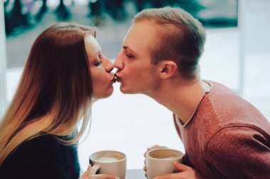 Hoş, esmer, sıcak kazak giyen, kafede buluşup telefona bakan ve onu kullanan bir çift. Soğuk sonbahar, kış ya da bahar günü, Avrupa şehri. Kapalı