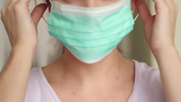 Mujer que pone máscara quirúrgica para la prevención del virus corona. Cierre de una joven en una máscara médica protectora, ella mira directamente. — Vídeos de Stock