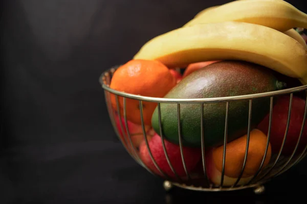 Tasty fruits in a metal basket. Wire basket with fruits on Black background. healthy eating concept