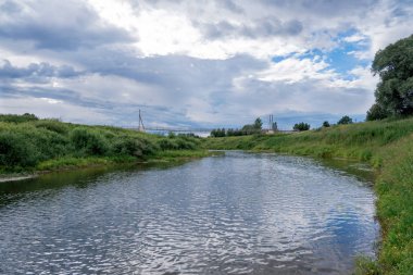 Mavi gökyüzü, Obsha nehri, yeşil kıyılar ve nehir üzerinde bir köprü. 
