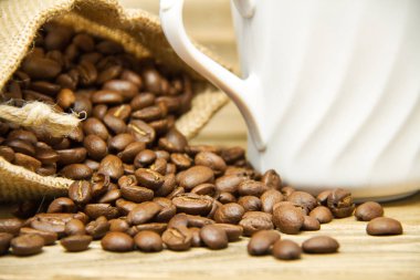 Kahve çekirdekleri bir çuval bezi çanta resimdeki beyaz kahve kupa parçası ile dökülen, yakın çekim.