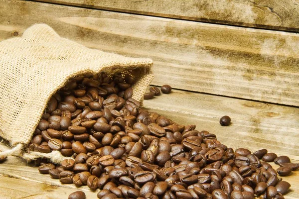I close up of a burlap bag of coffee beans spilled onto a wood table with a texture applied around the edges of the image.