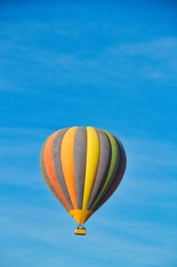 Parçalı bulutlu gökyüzü altında yükselen bir sıcak hava balonu.