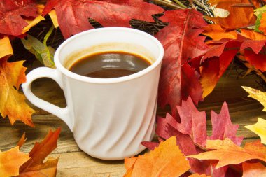 Ahşap bir yüzey üzerinde sonbahar renkleri yaprakları ile çevrili tek bir sıcak fincan kahve.