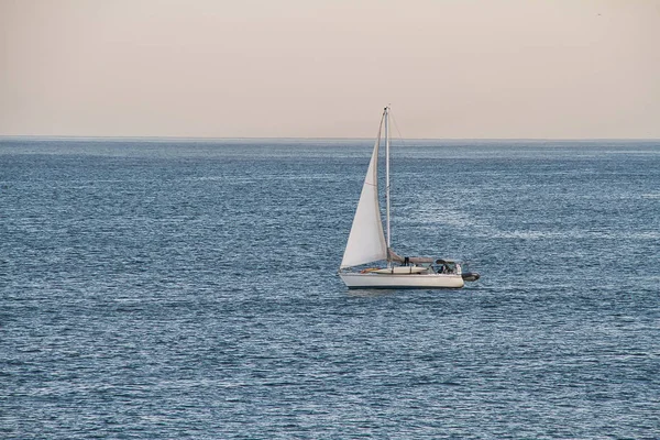 A sailboat at sea in the open ocean in the late afternoon.