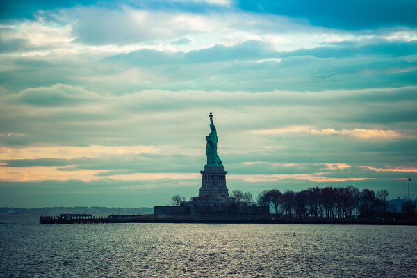 The Statute of Liberty standing in New York harbor during sunset.