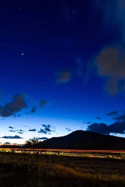 Evening image of the desert night sky during the blue hour with dramatic clouds and stars with a mountain landscape.