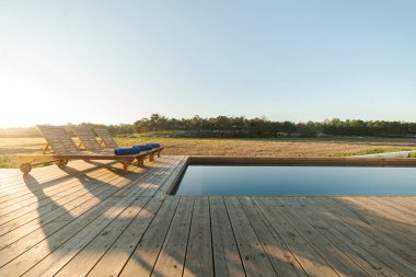 Modern villa havuzunda ahşap şezlonglar.