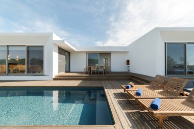 Modern villa havuzunda ahşap şezlonglar.