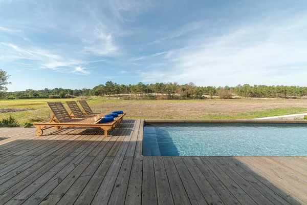 Wooden lounge chairs in modern villa pool and deck