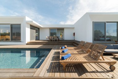 Modern villa havuzunda ahşap şezlonglar.