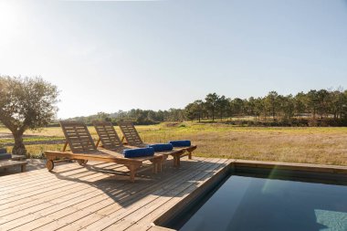 Modern villa havuzunda ahşap şezlonglar.