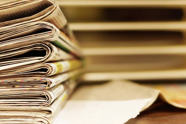 Folded newspapers stacked in a pile on blurred background, side view, selective focus