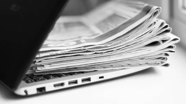 Newspapers and laptop. Personal computer and pile of daily papers with news. Information on screen or paper. Fresh data, old fashioned journals and modern technology. Business sources, selective focus