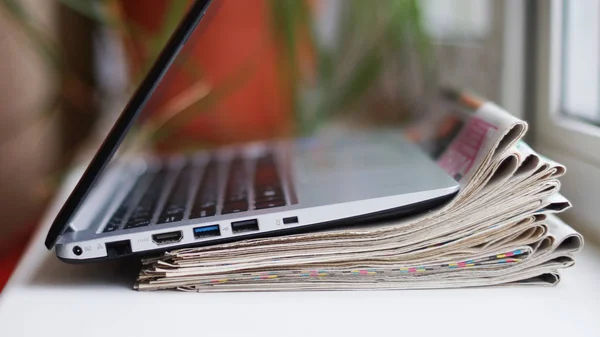 Newspapers and laptop. Personal computer and pile of daily papers with news. Information on screen or paper. Fresh data, old fashioned journals and modern technology. Business sources, selective focus