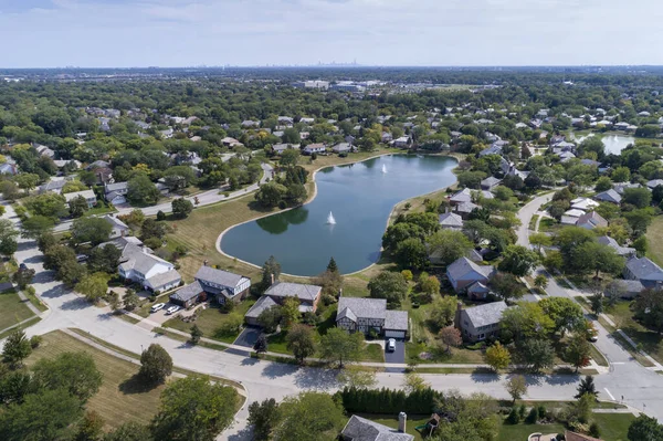 空中俯瞰着郊区一个有池塘的绿树成荫的社区 以及远处的芝加哥市中心 — 图库照片