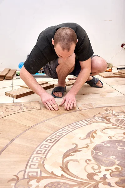 The carpenter installs one of the decorative elements of the parquet. — Stock Photo, Image