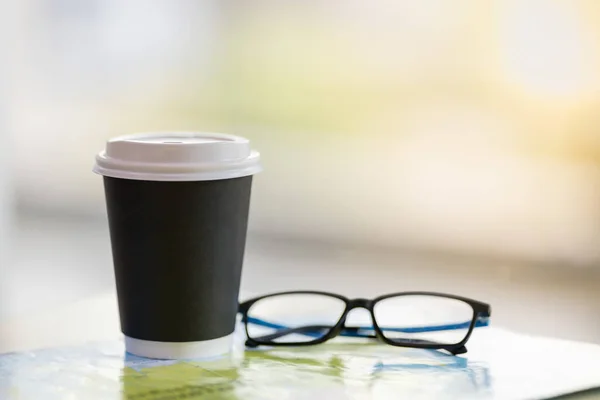 Κοντινό πλάνο της take away χάρτινο φλιτζάνι ζεστό καφέ με γυαλί ανάγνωσης — Φωτογραφία Αρχείου