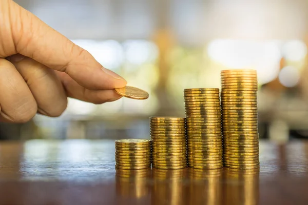 Business, Money, Finance and Saving Concept. Close up of man hand holding and put a coin to stack of coins on wooden table.