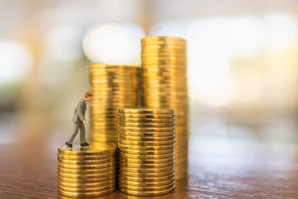 Business, Money Investment and Planning Concept.  Close up of businessman miniature people figure walking on top of stack of gold coins on wooden table with copy sapce.