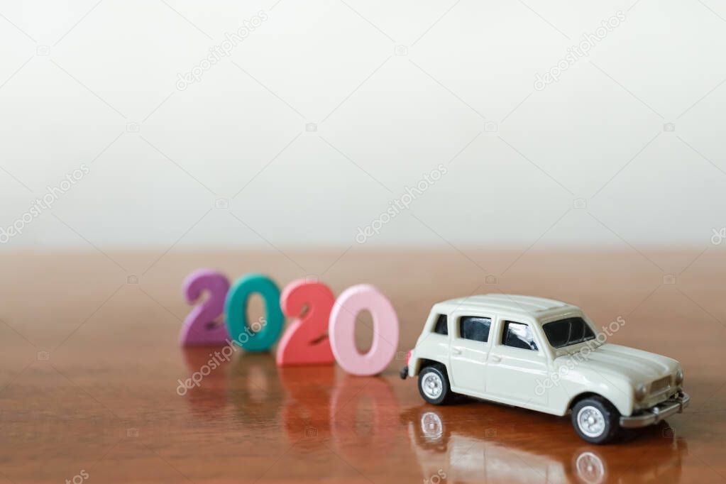 2020 New year and Business Concept. CLose up of miniature white car with wooden colrful number on wood table with copy space