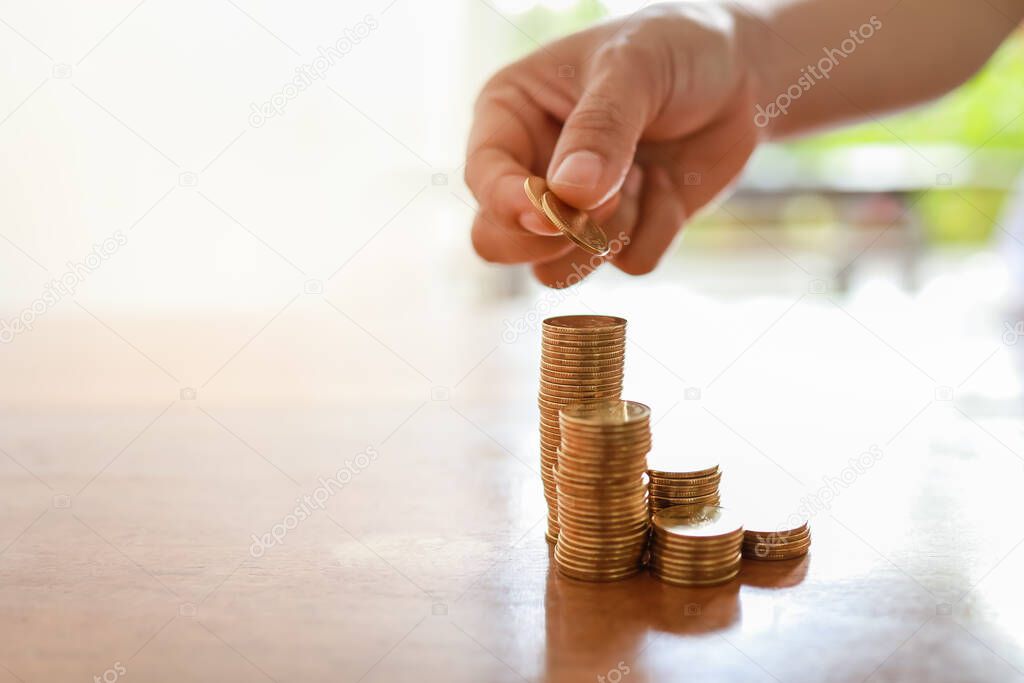 Business, Money, Finance, Secure and Saving Concept. Close up of woman hand holding and put two coins to stack of coins on wooden table with copy space.