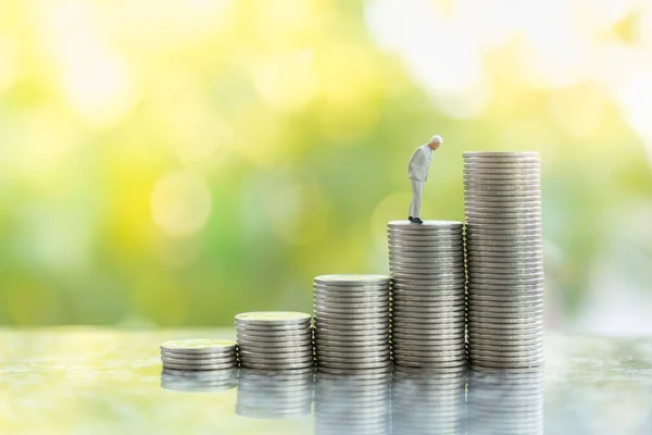 Business, Money Investment and Planning Concept.  Close up of businessman miniature people figure standing on stack of silver coins with green anture background with copy sapce.