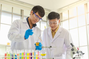 Asyalı uzman doktor bilim adamına yakın çekim, Asyalı genç bilim adamına çalışma laboratuarında pipette test ve araştırma yapmasını öğretmek ve rehberlik etmek. Sağlık, Coronavirus (Covid-19) Koruma Konsepti.