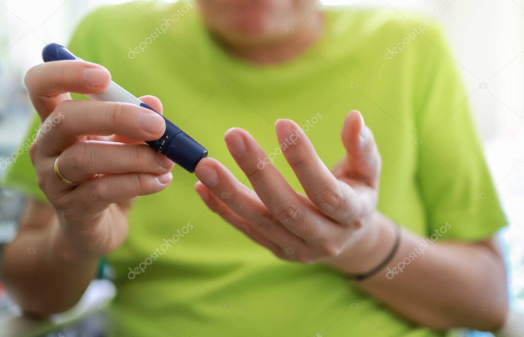 Close up of man hands using lancet on finger to check blood sugar level by Glucose meter in bedroom in the morning. Use as Medicine, diabetes, glycemia, health care and people concept.