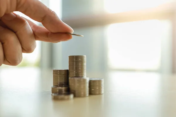 Business, Money, Finance, Secure and Saving Concept. Close up of man hand holding and put coins to top of stack of coins on wooden table.