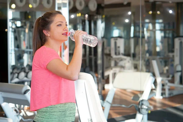 Sports woman with a bottle of water and a towel around her neck. Break after workout in the gym. The concept of health and sport.